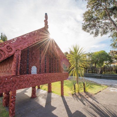 Ornate red wooden structure with carvings under trees, sun shining through.