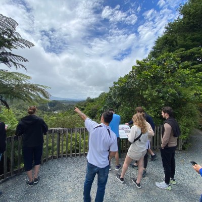 Group of people at a lookout point with greenery and a cloudy sky.