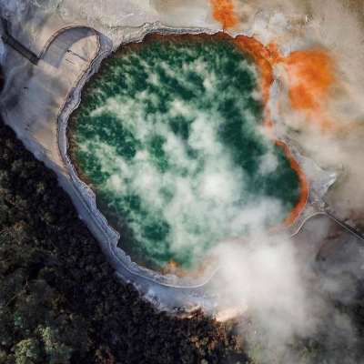 Aerial view of a steaming hot spring with green water and orange edges.