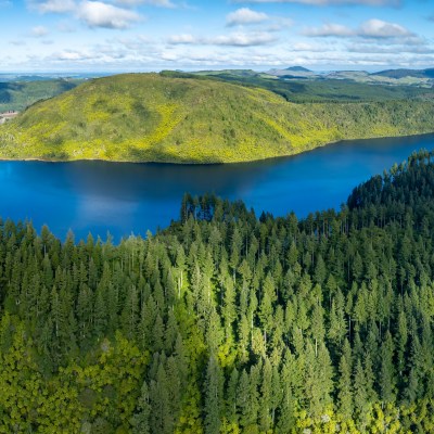 Aerial view of a lush green forest surrounding a large blue lake under a partly cloudy sky.