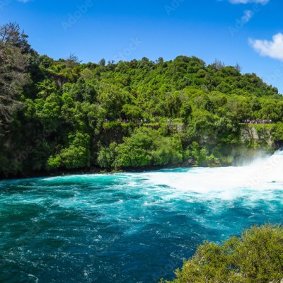 Blue river with rapids surrounded by lush green forest under a clear blue sky.