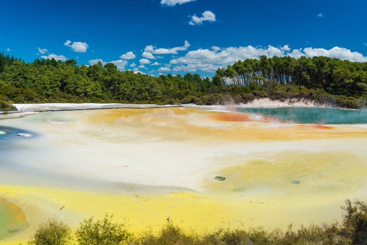 Vibrant geothermal lake with colorful mineral deposits and surrounding forest.