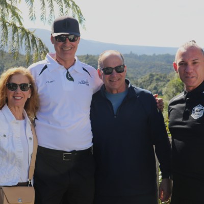 Four people posing outdoors with greenery and mountains in the background.