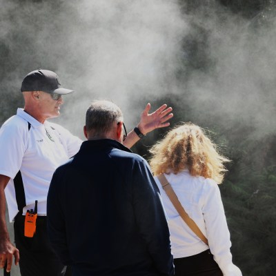 Three people in misty outdoor setting, one gesturing with hand.