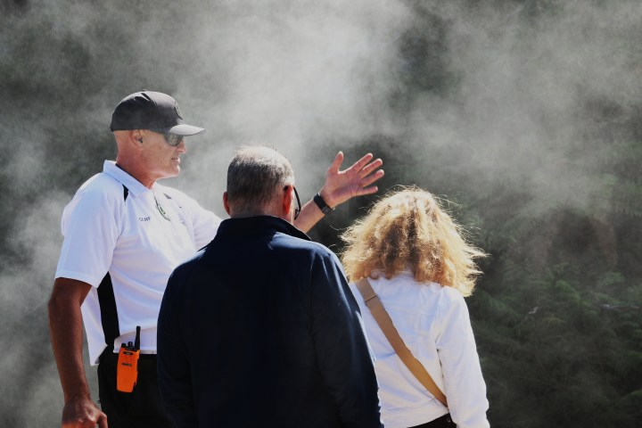 Three people in misty outdoor setting, one gesturing with hand.