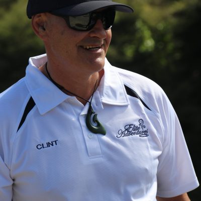 Person in a white polo, sunglasses, and cap outdoors, smiling.