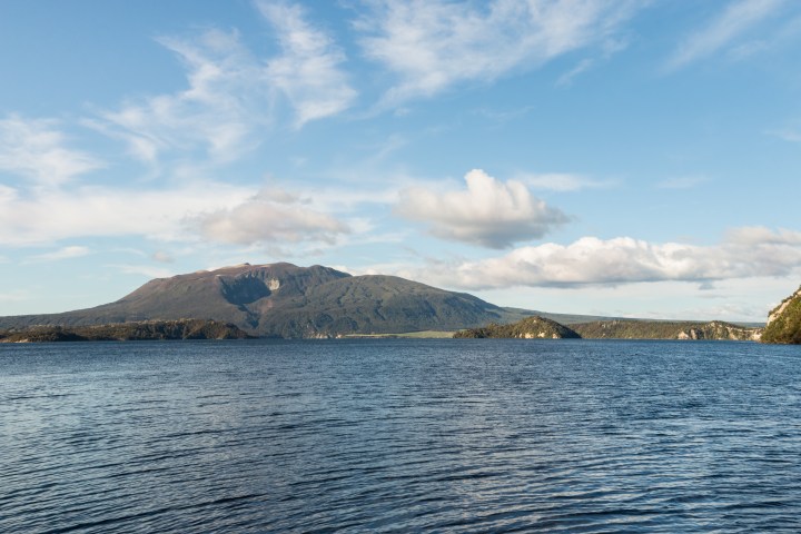 Scenic view of a calm lake with a mountain under a partly cloudy sky.