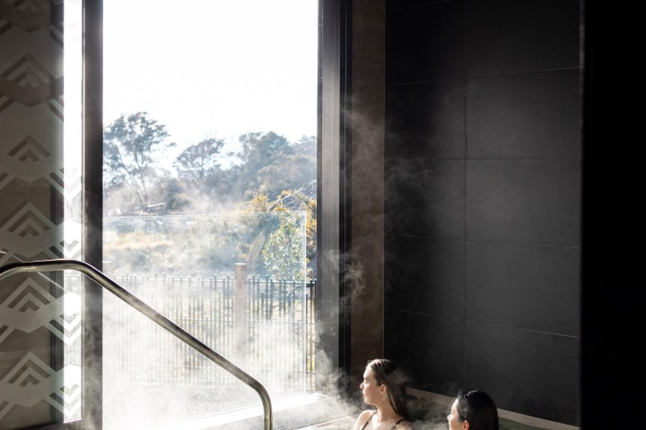 Two people relaxing in an indoor hot tub near a large open window.